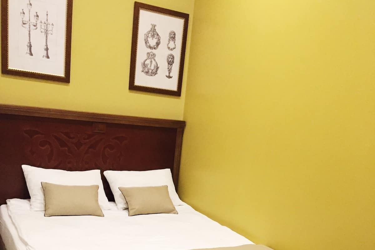 A neatly made bed with two pillows and a beige bedspread in a room with yellow walls and a wooden headboard.