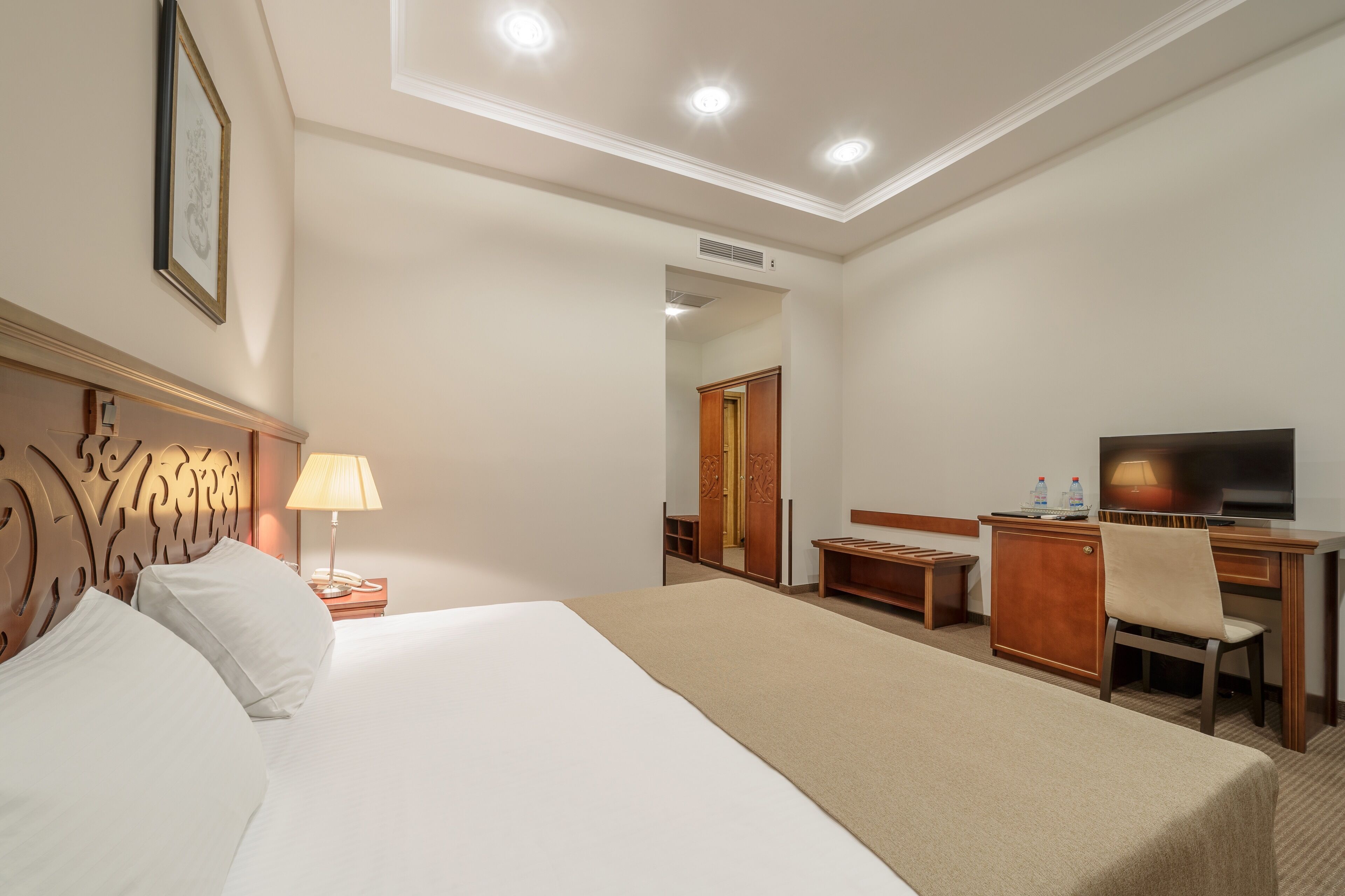 A hotel room with a large bed, a desk with a chair, a TV, and a wardrobe.