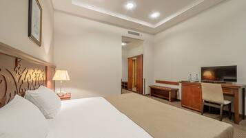 A hotel room with a large bed, a desk with a chair, a TV, and a wardrobe.