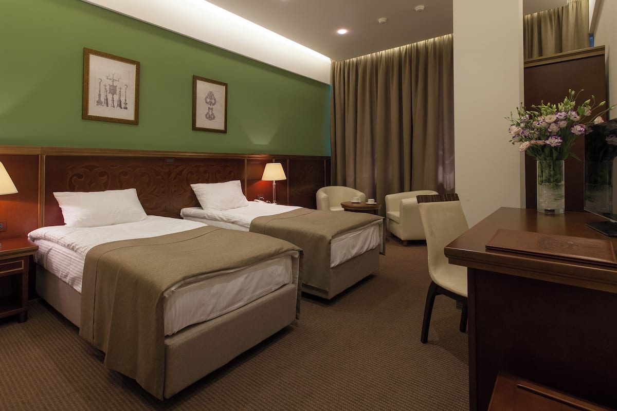 A hotel room with two beds, a desk, a chair, and a vase of flowers.