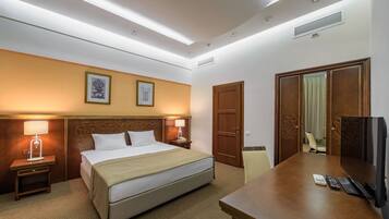 A hotel room with a bed, bedside lamps, a desk with a TV, and a door.