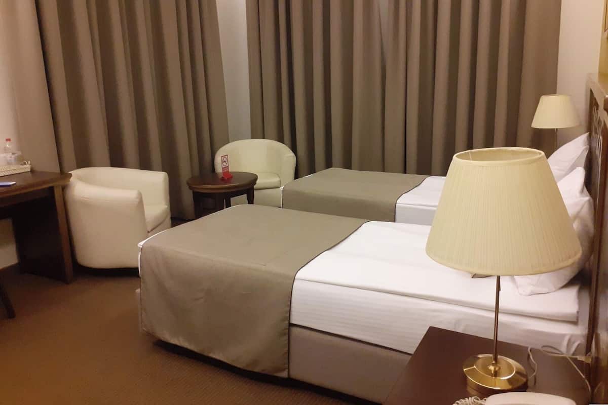 A hotel room with two beds, a desk, a chair, a lamp, and curtains.