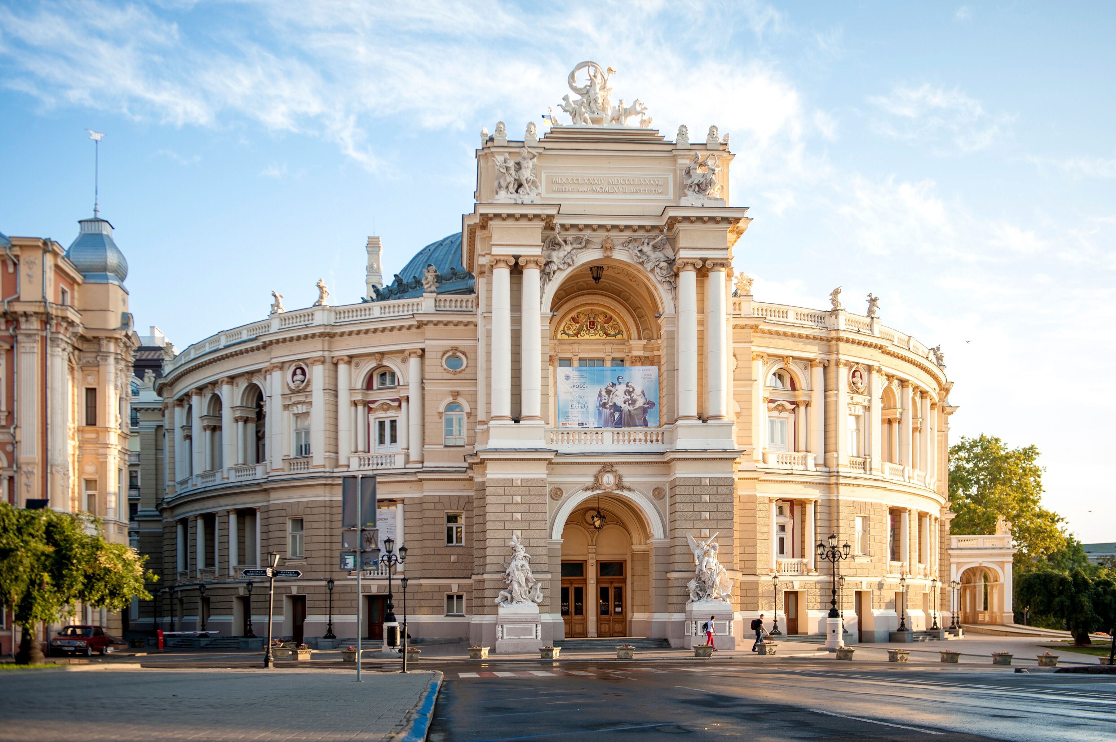 A grand, historic building with classical architecture, featuring a central entrance with a large arch and statues, surrounded by columns and ornate decorations.