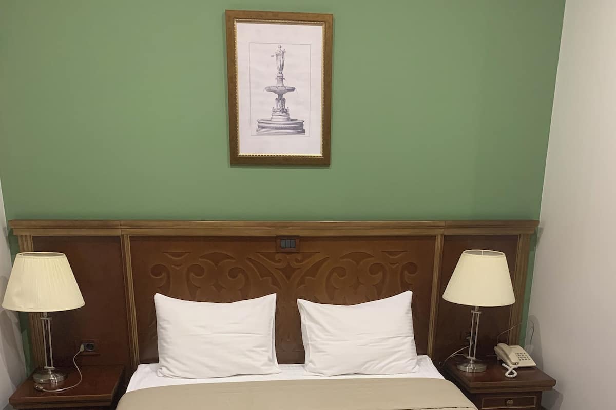 A hotel room with a large bed, two nightstands, a framed picture on the wall, and a wooden headboard.