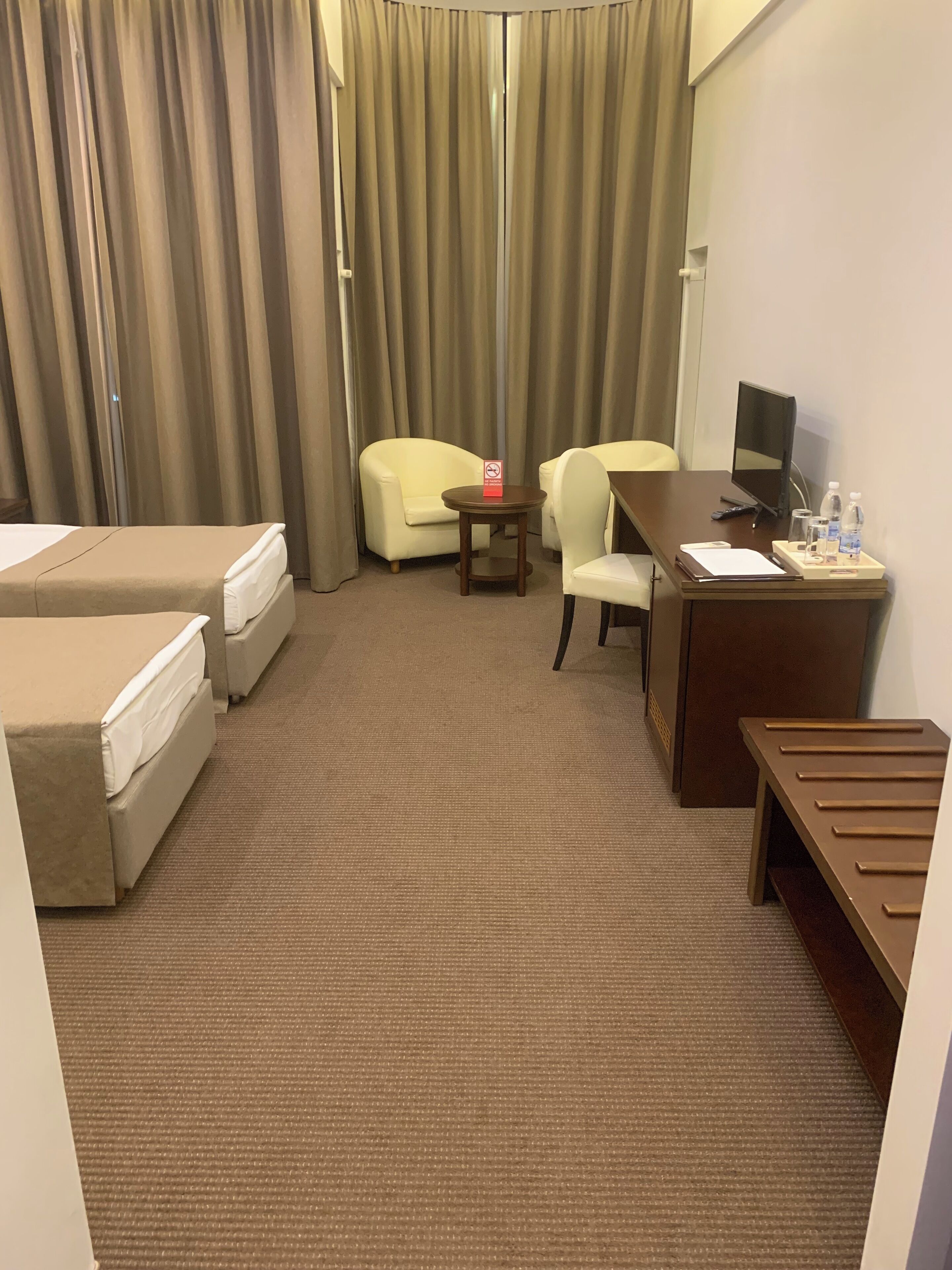 Une chambre d’hôtel avec deux lits simples, un bureau avec un ordinateur, une chaise, une petite table et un téléviseur.