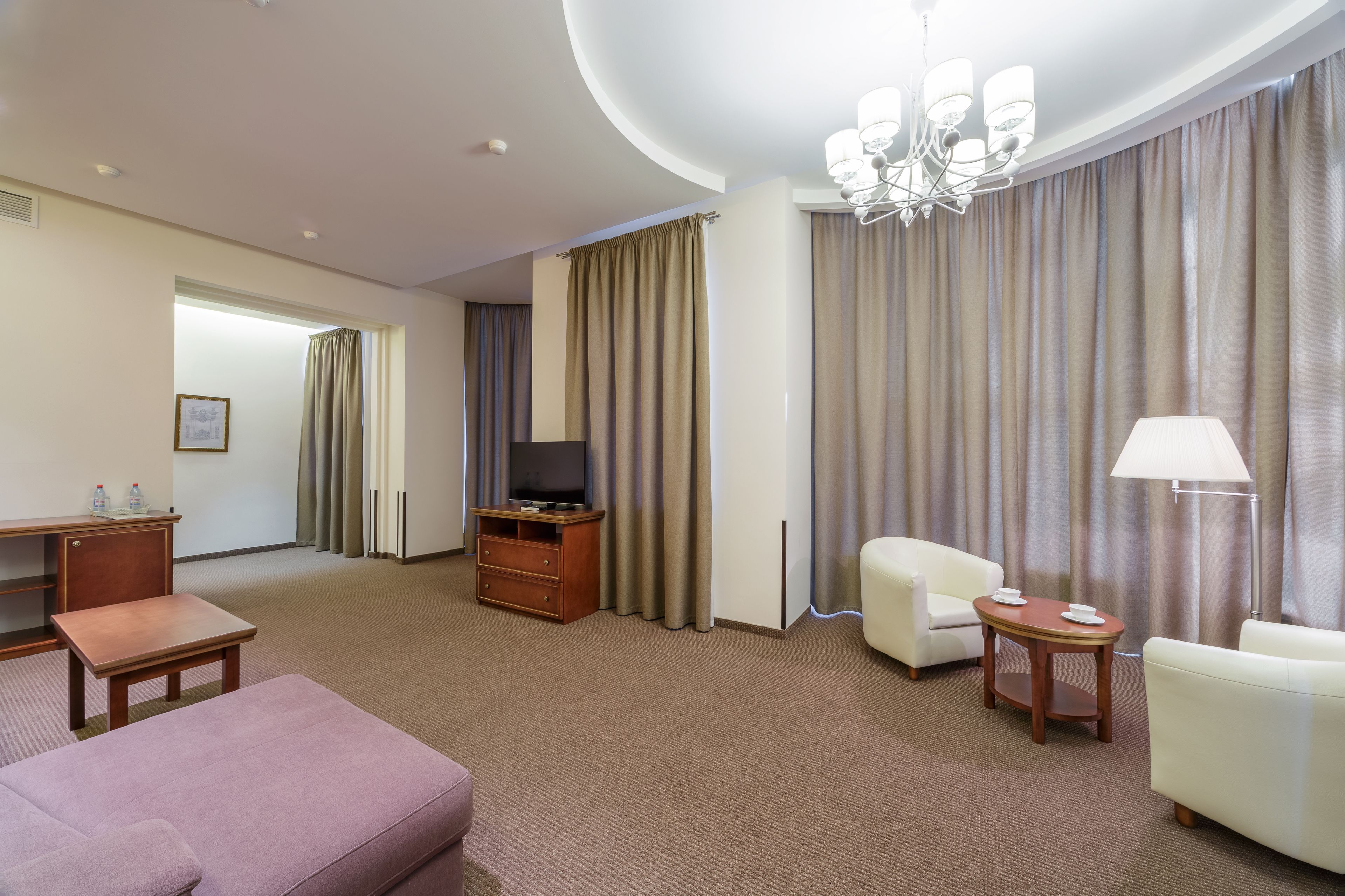 Habitación de hotel con televisión de pantalla plana, escritorio de madera, una mesita, sofá, silla y lámpara.