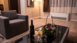 A modern living room with a sofa, a glass coffee table with wine glasses and a bottle, and a decorative flower arrangement. - Hotel Opera House (Skopje)