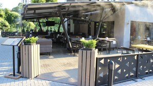 An outdoor seating area with tables and chairs, a covered patio, and a signboard. - Hotel Opera House (Skopje)