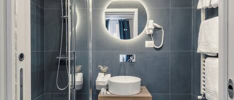 Een moderne badkamer met een douchecabine van glas, een ronde spiegel, een wastafel en een toilet.