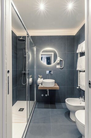 A modern bathroom with a glass-enclosed shower, a round mirror, a sink, and a bidet.