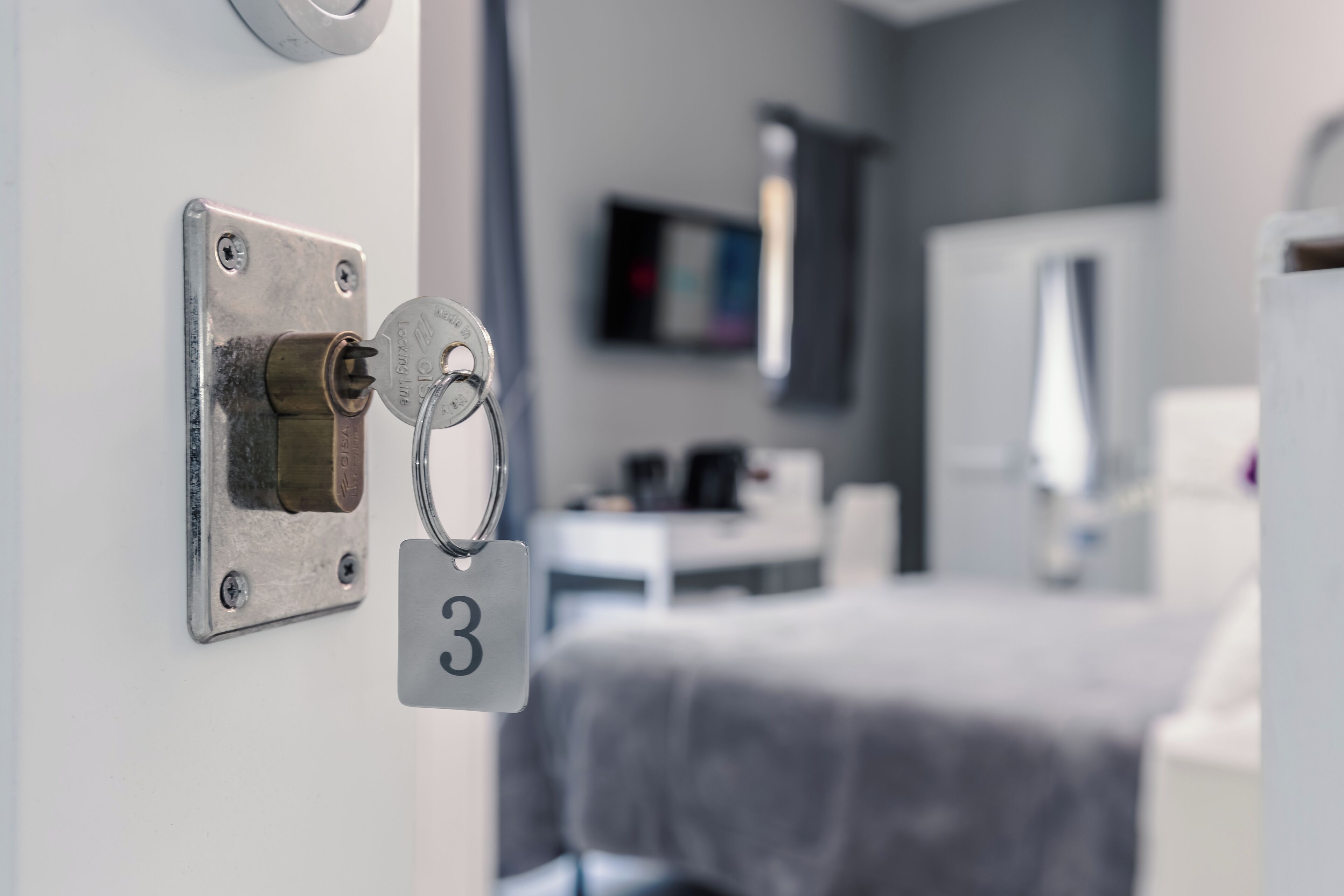 Une chambre d’hôtel avec un lit, un téléviseur fixé au mur et une serrure de porte avec une clé et une plaque indiquant le numéro de la chambre.