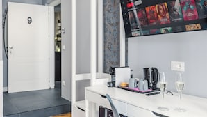 A hotel room with a white desk, a coffee maker, two glasses of wine, and a TV displaying movie posters. - Bed and Best (Rome)