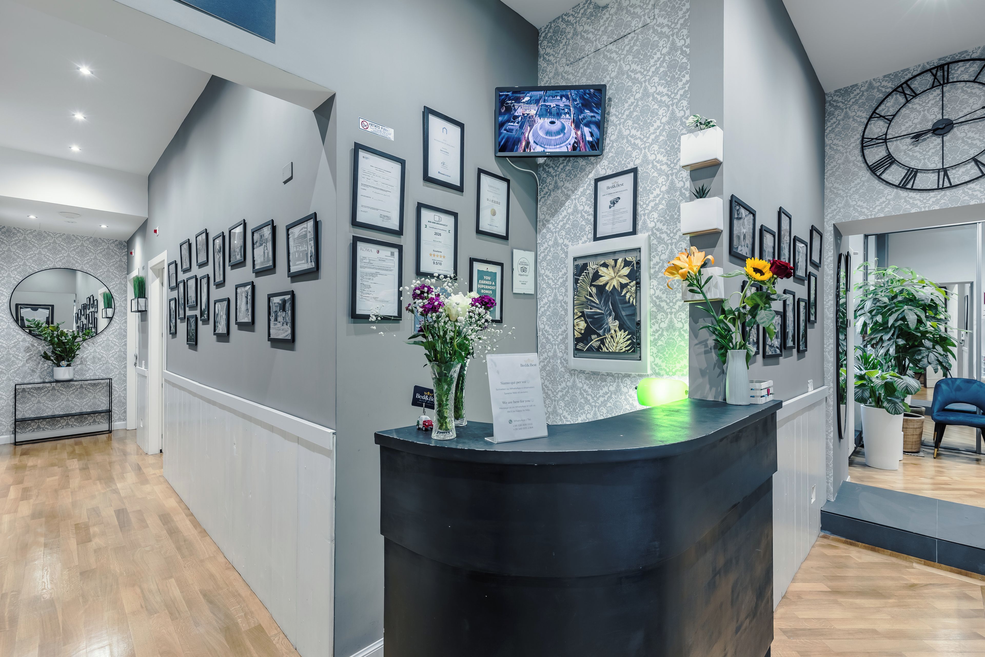 A reception area with framed certificates on the wall, a TV mounted above the reception desk, and a clock on the wall.