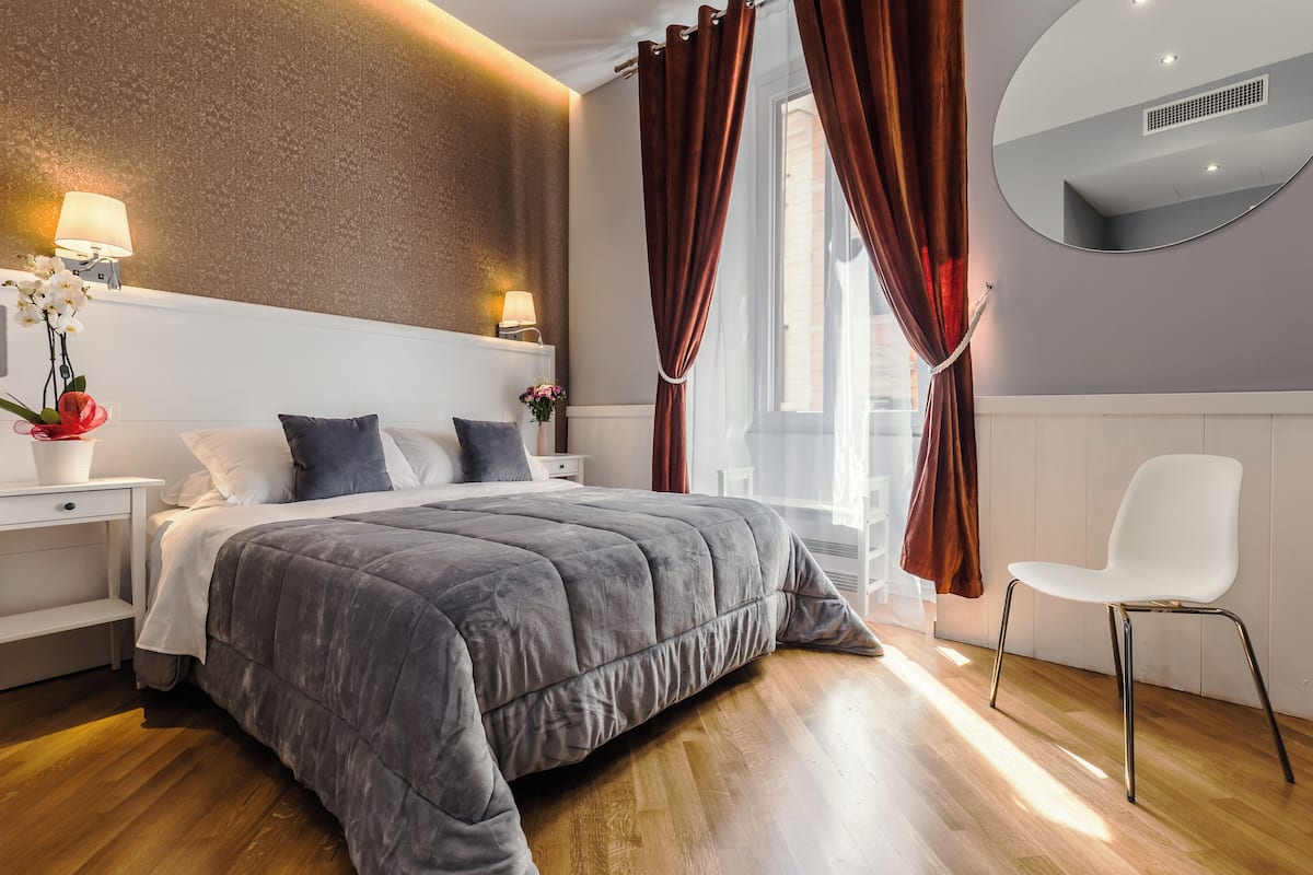 Ein modernes Schlafzimmer mit einem großen Bett, einem Nachttisch mit Lampe, einem Sessel und einem Fenster mit Vorhängen.