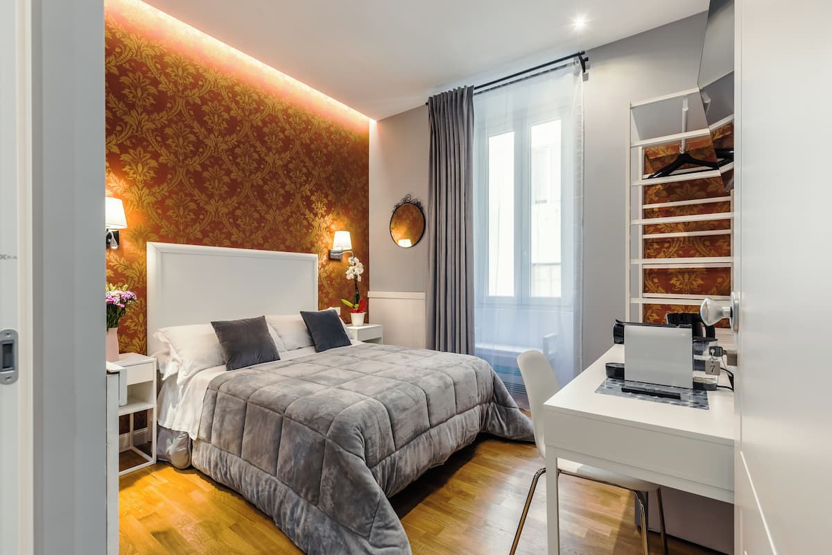 Ein modernes Hotelzimmer mit einem großen Bett, einem Schreibtisch mit Laptop, einem Kleiderschrank mit Kleidung und einem Fenster mit Vorhängen.