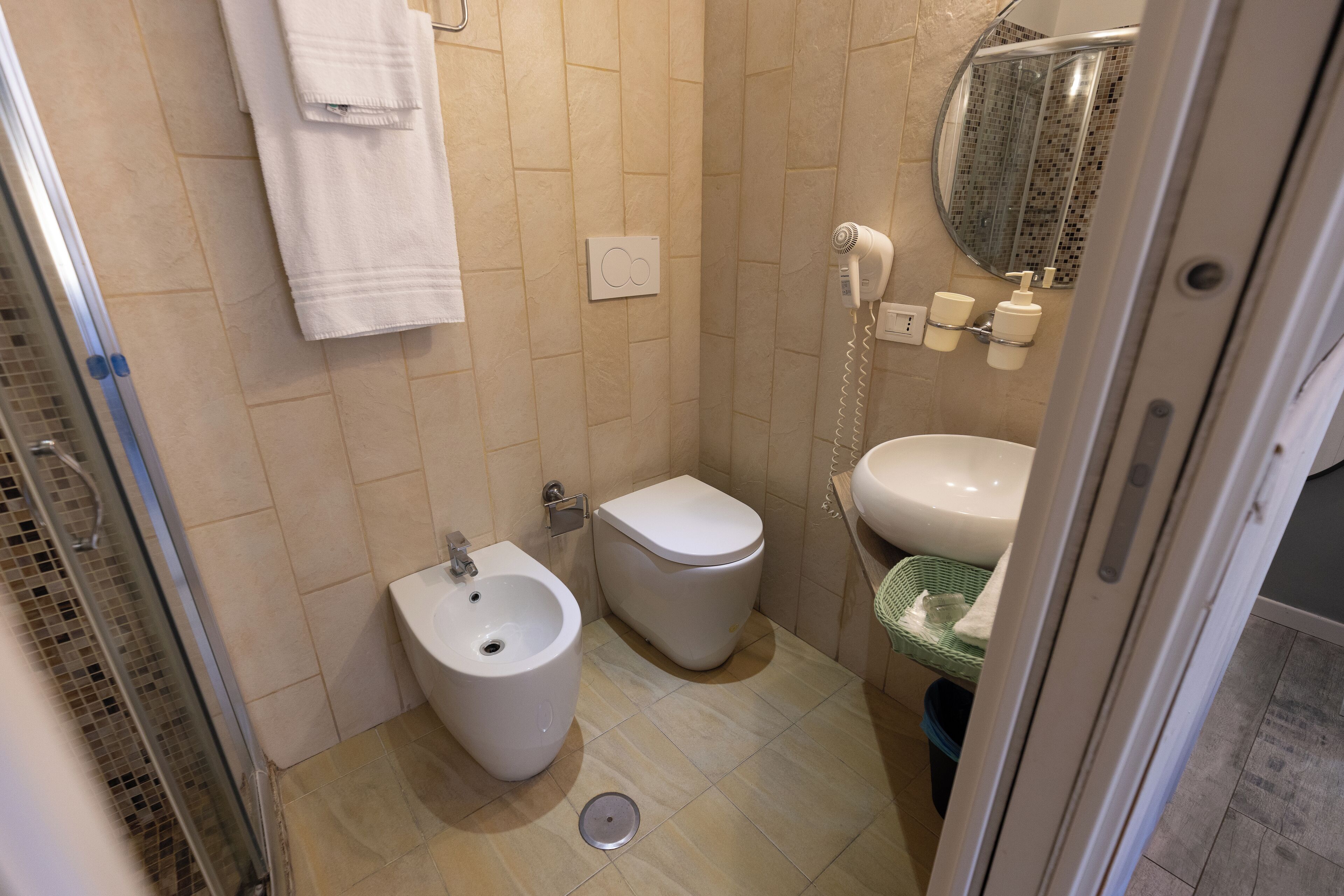 A small bathroom with a bidet, toilet, sink, and a shower area.