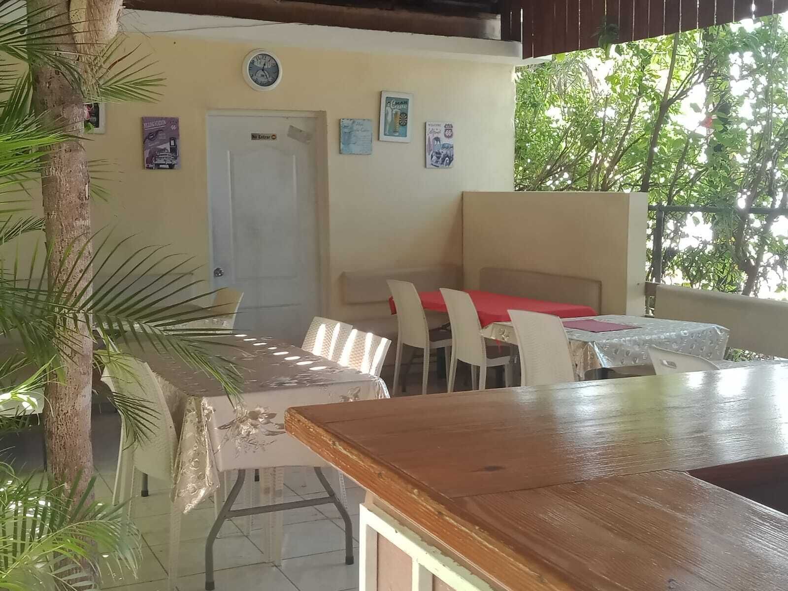 A covered outdoor dining area with tables and chairs, a wooden counter, and a door.