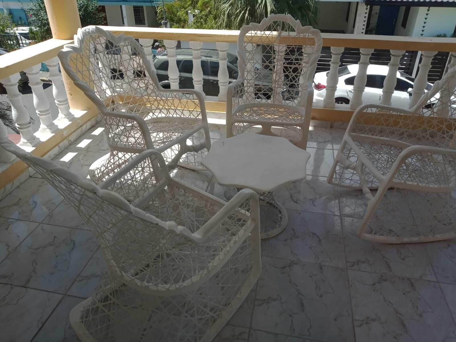 A balcony with white wicker chairs and a small table, surrounded by a white balustrade.