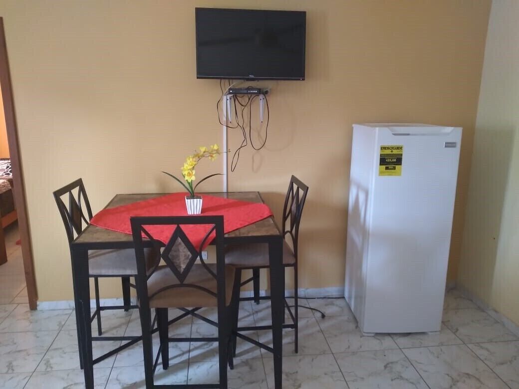 A dining area with a table and chairs, a television mounted on the wall, and a refrigerator.