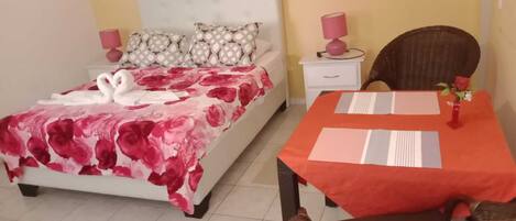 Una habitación de hotel con una cama, una mesa de comedor con sillas, una mesita de noche y una lámpara.