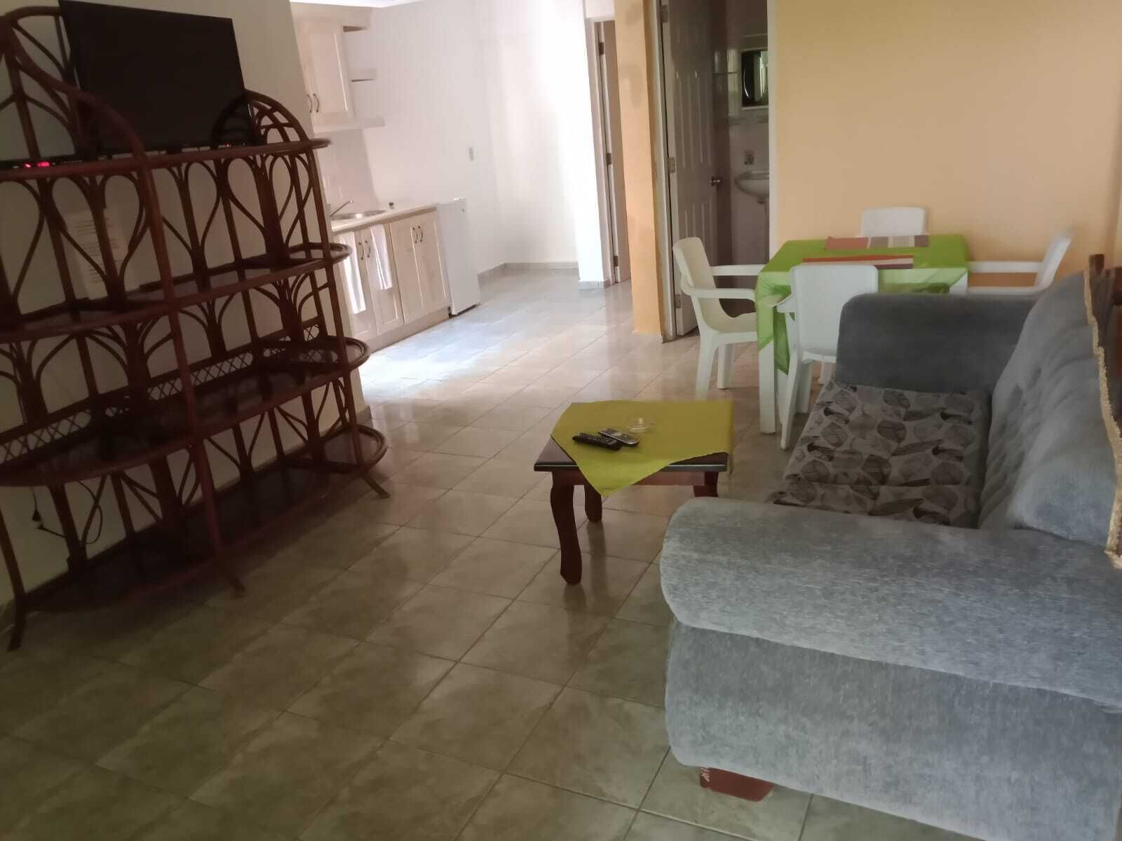 Ein Wohnzimmer mit Sofa, Couchtisch und einem TV-Schrank. Es gibt einen Essbereich mit Tisch und Stühlen.