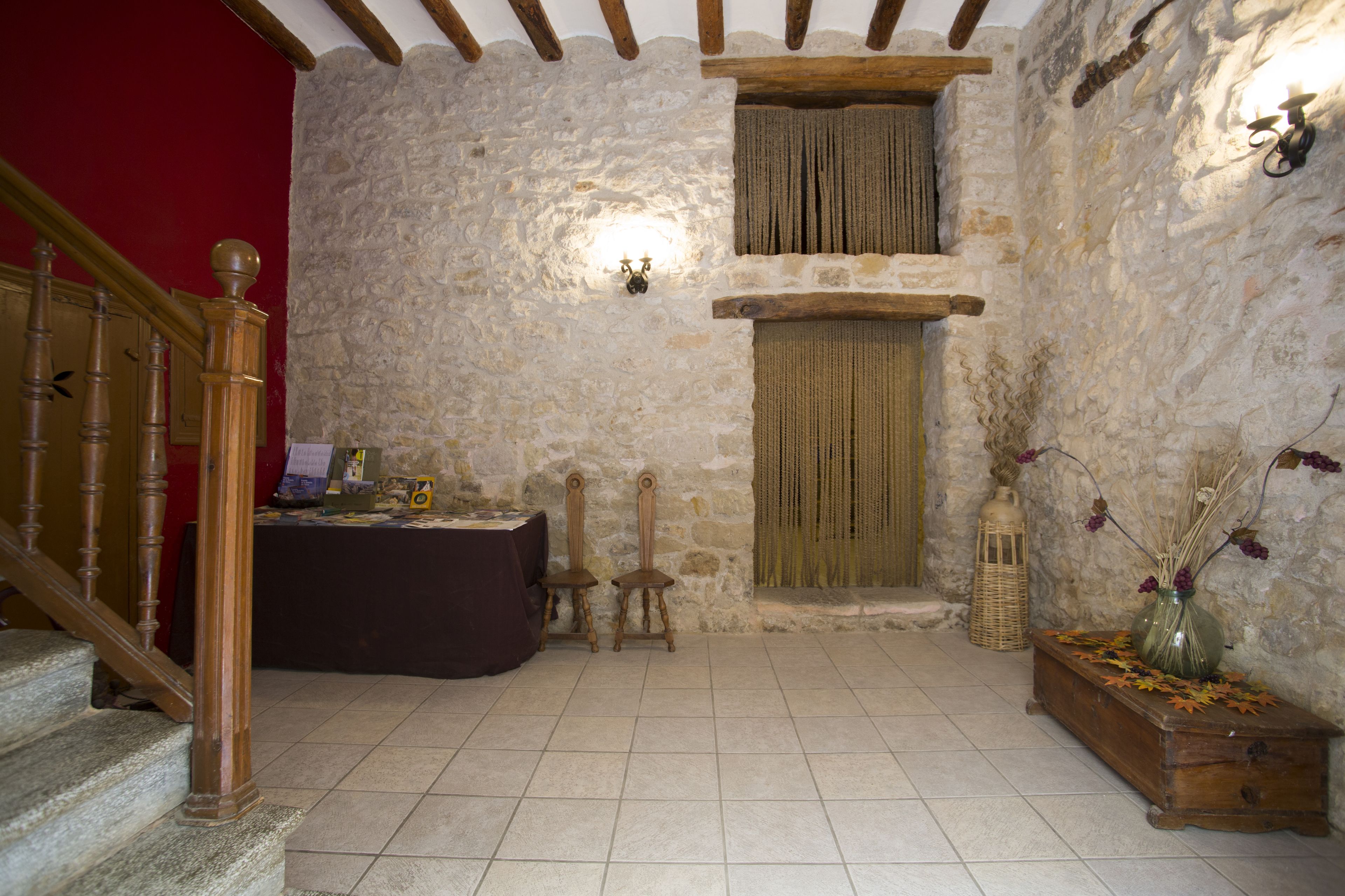 A rustic room with stone walls, a wooden staircase, a table with a dark cloth, and a wooden bench with decorative items.