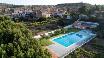 Una piscina con un deck circundante, un área con césped y vistas a una colina con edificios.