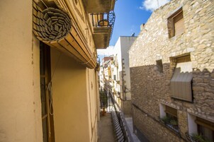 Un estrecho callejón entre edificios con fachadas de piedra, una puerta de madera y una barandilla de metal.