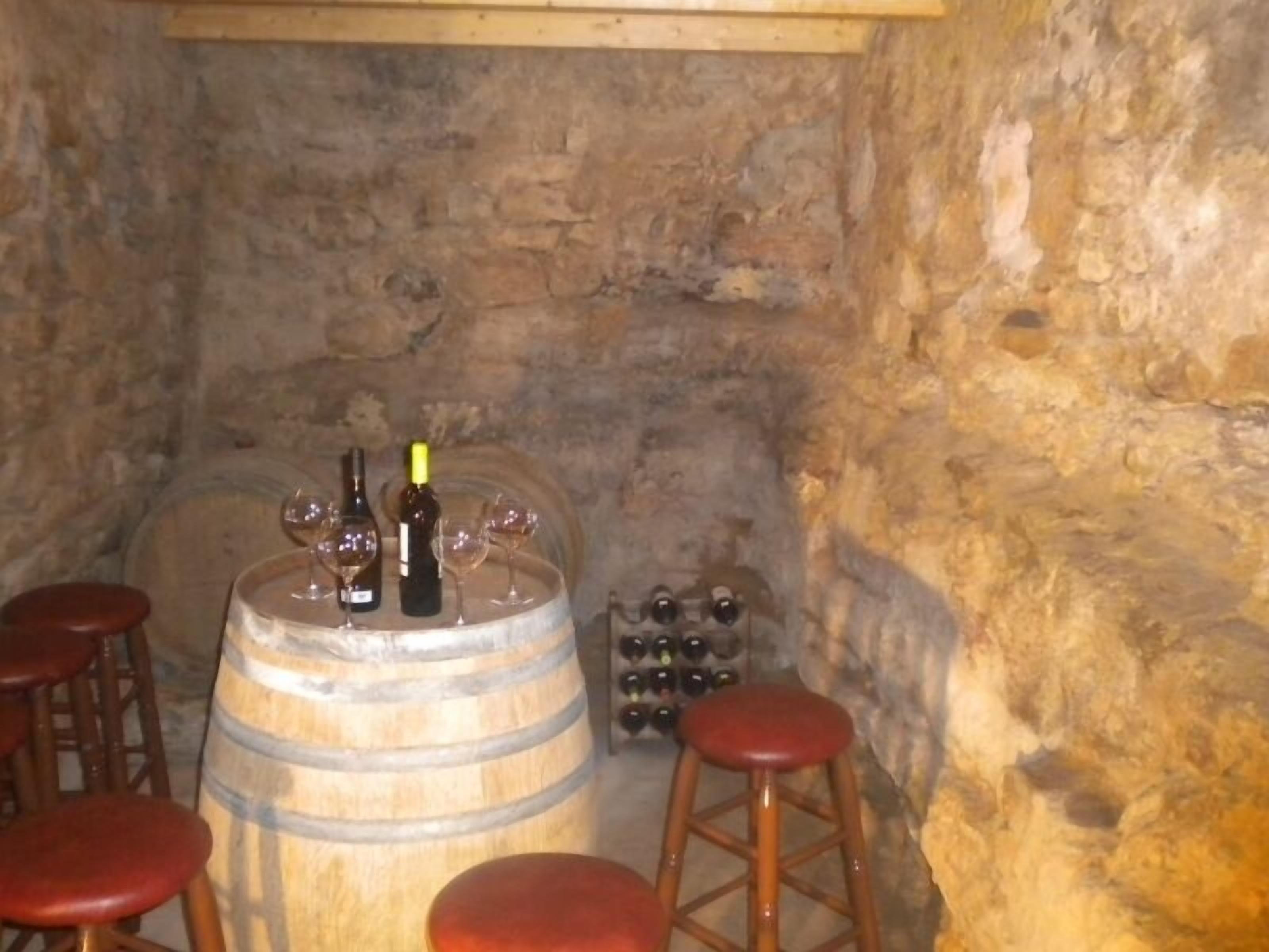 Une cave rustique avec des barils en bois, des bouteilles de vin et des tabourets.