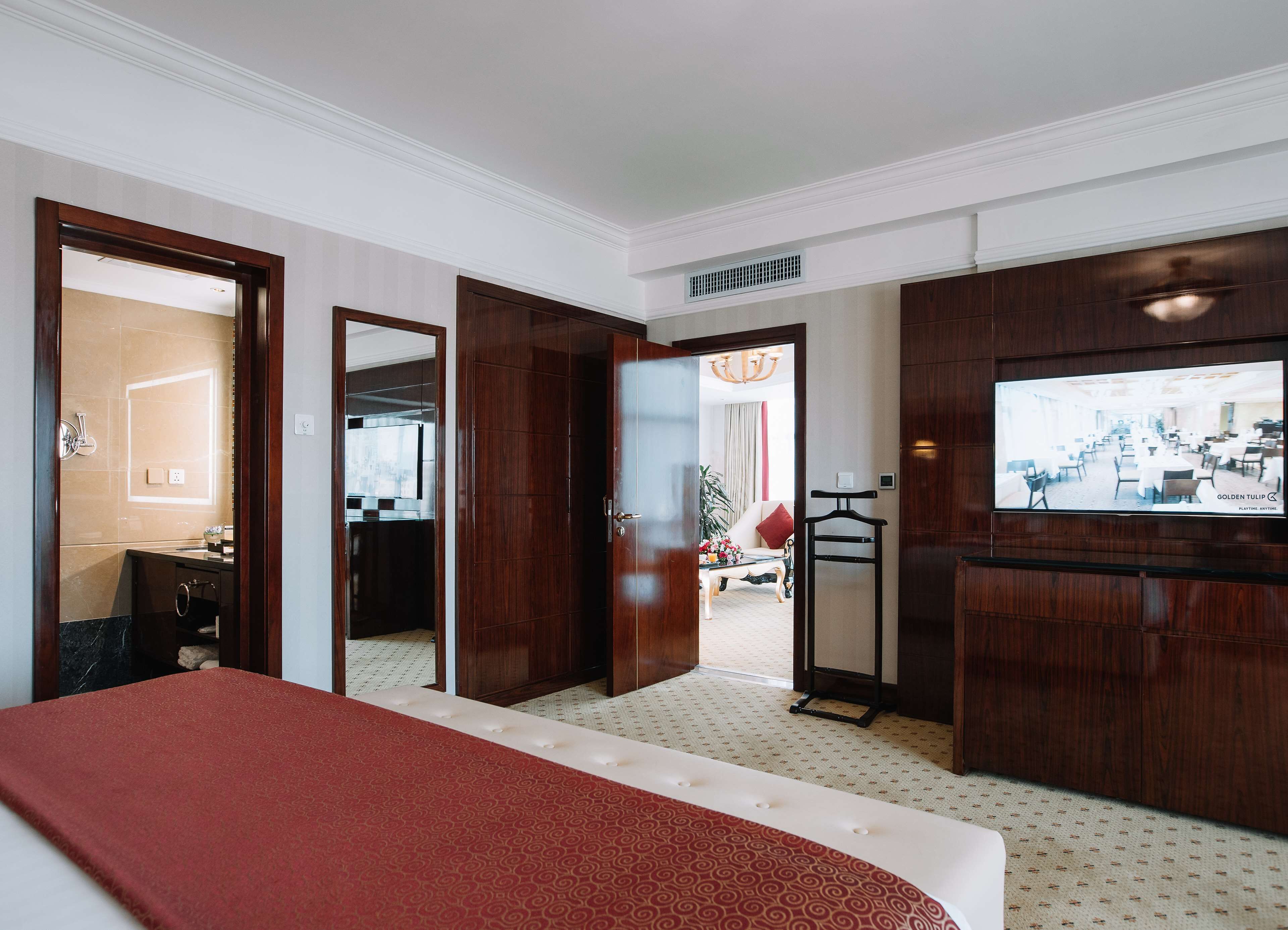 A hotel room with a large bed, a TV mounted on the wall, a bathroom with a mirror, and a view of the dining area.