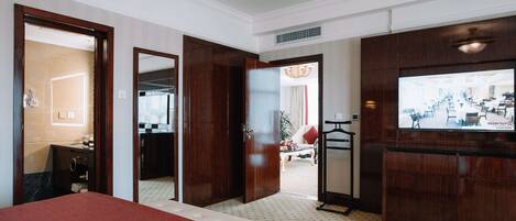 A hotel room with a large bed, a TV mounted on the wall, a bathroom with a mirror, and a view of the dining area.