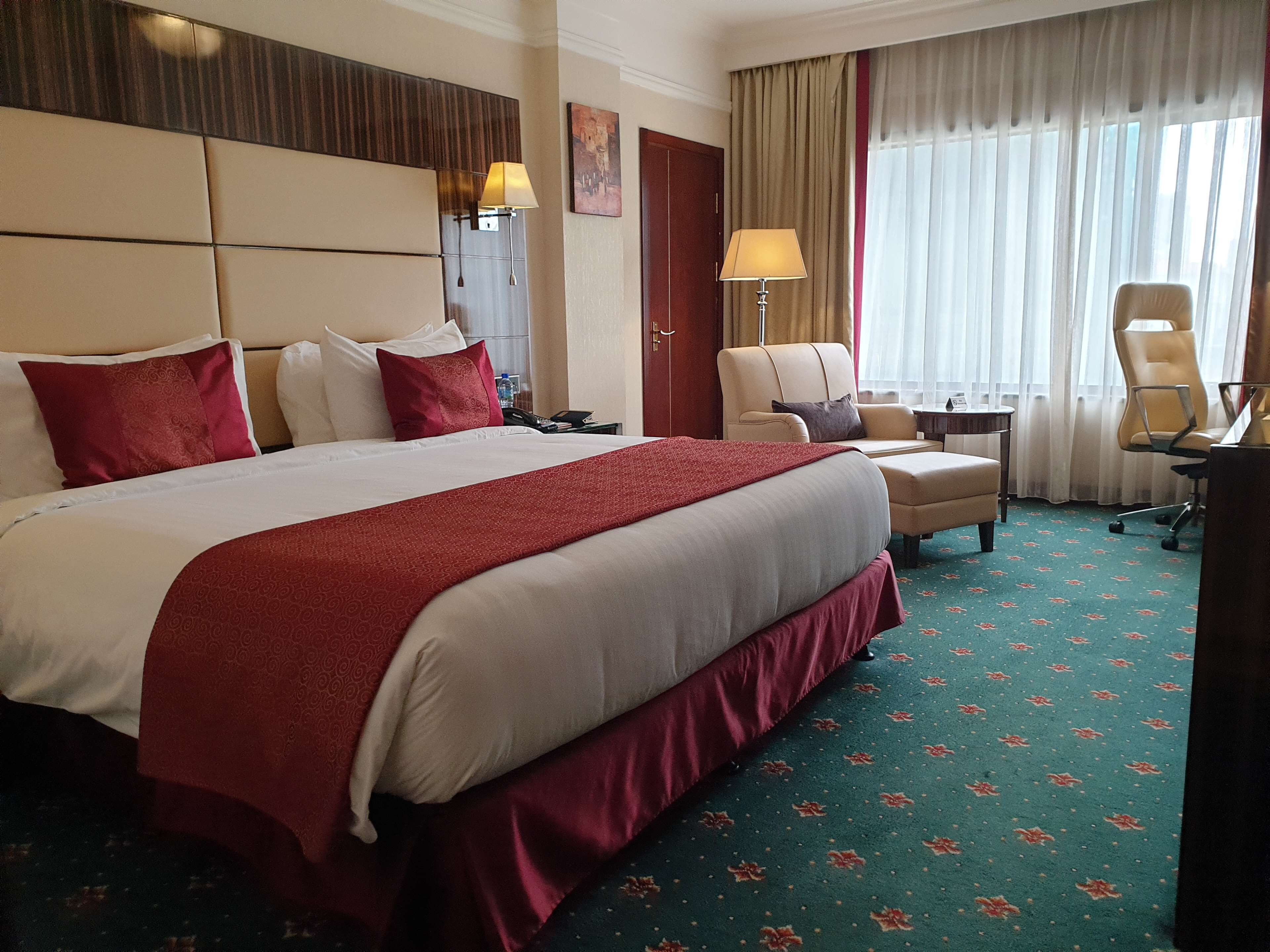 Una habitación de hotel con una cama grande, un escritorio, una silla y un ventanal con cortinas.