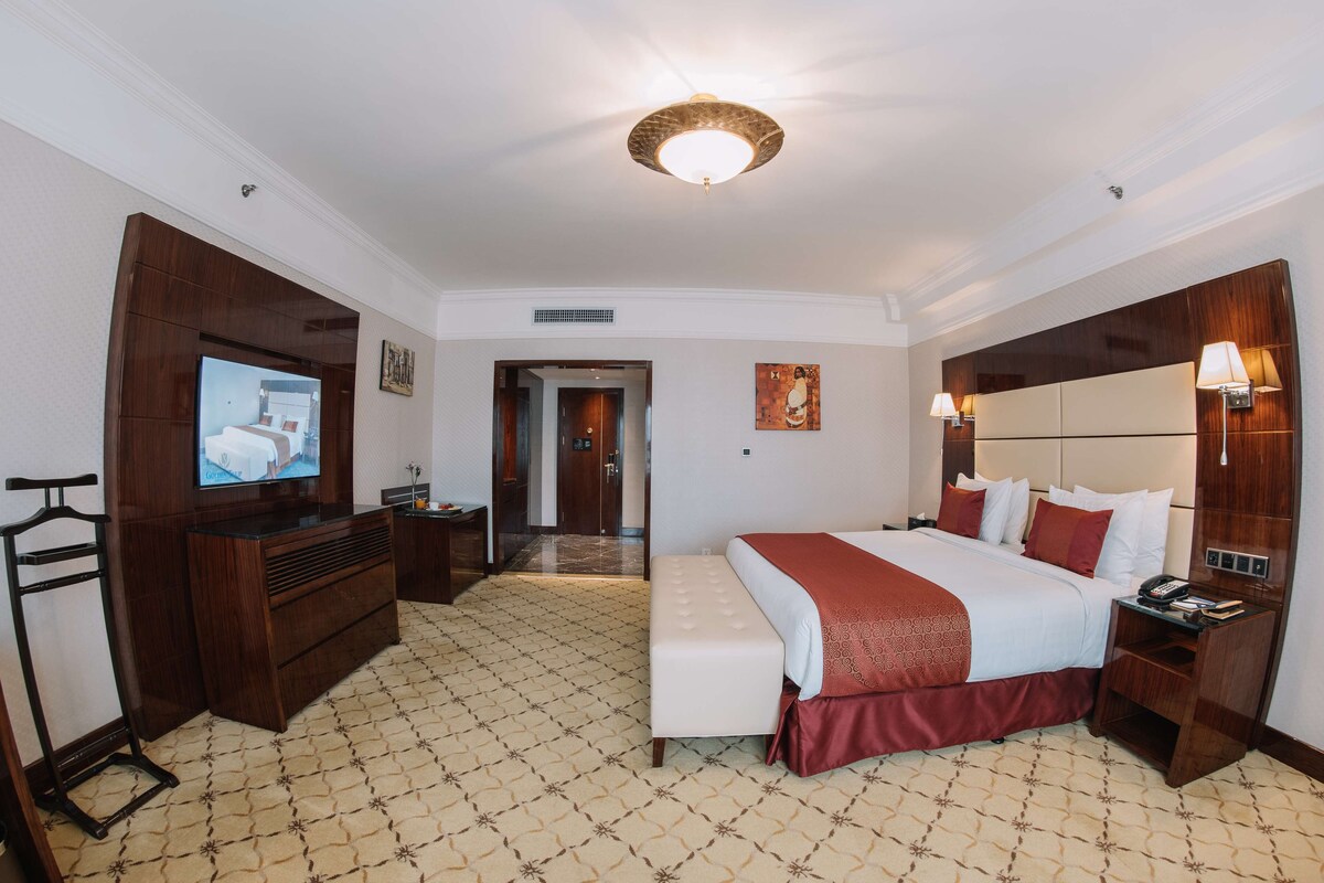 A hotel room with a large bed, a TV, a desk, and a wardrobe.