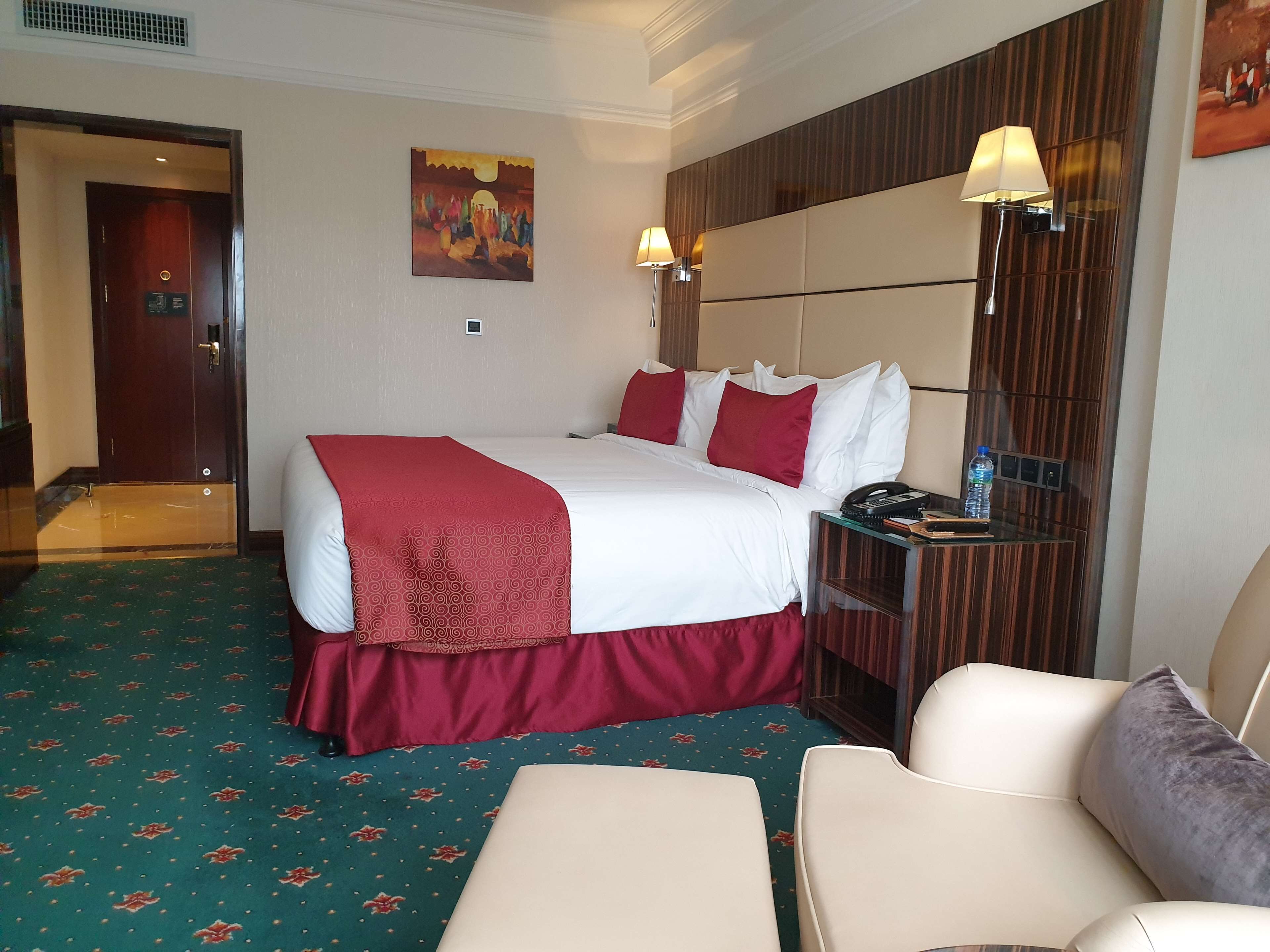 Camera d'albergo con un letto grande, un comodino con una lampada, una sedia e un quadro appeso al muro.