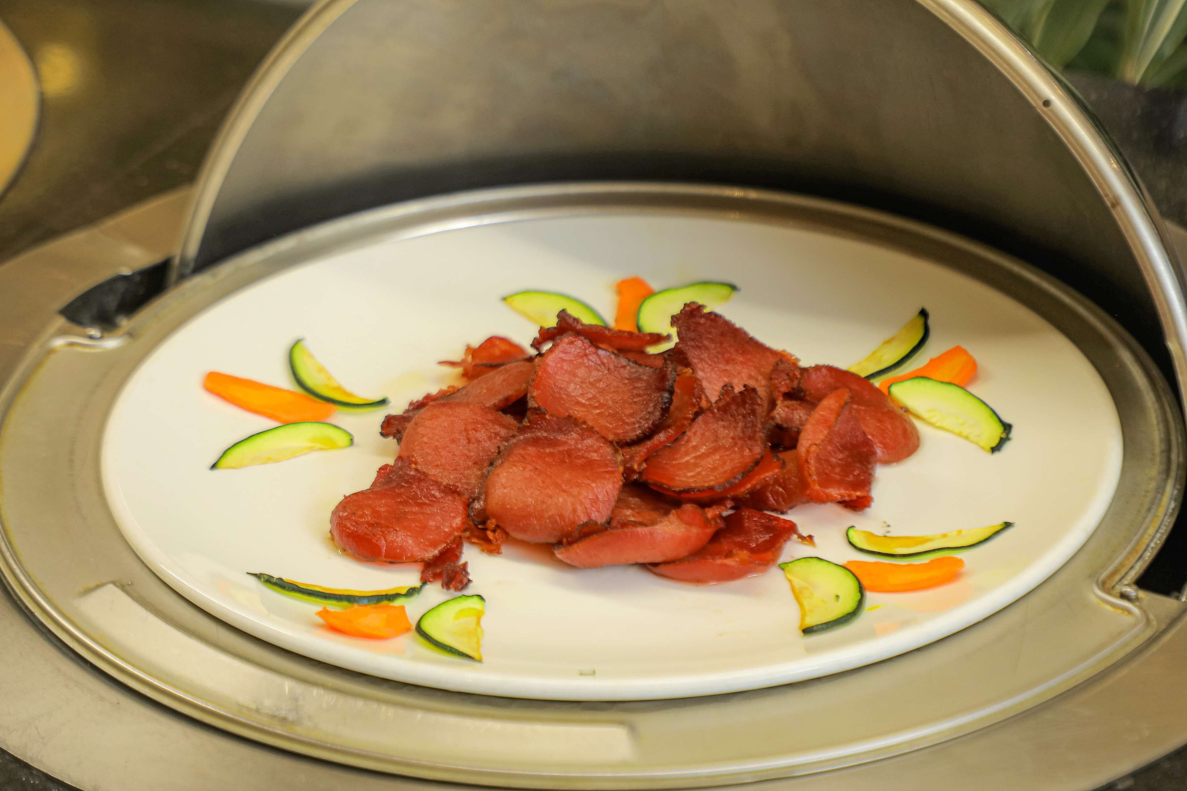 A plate of sliced meat with vegetables on a white plate.