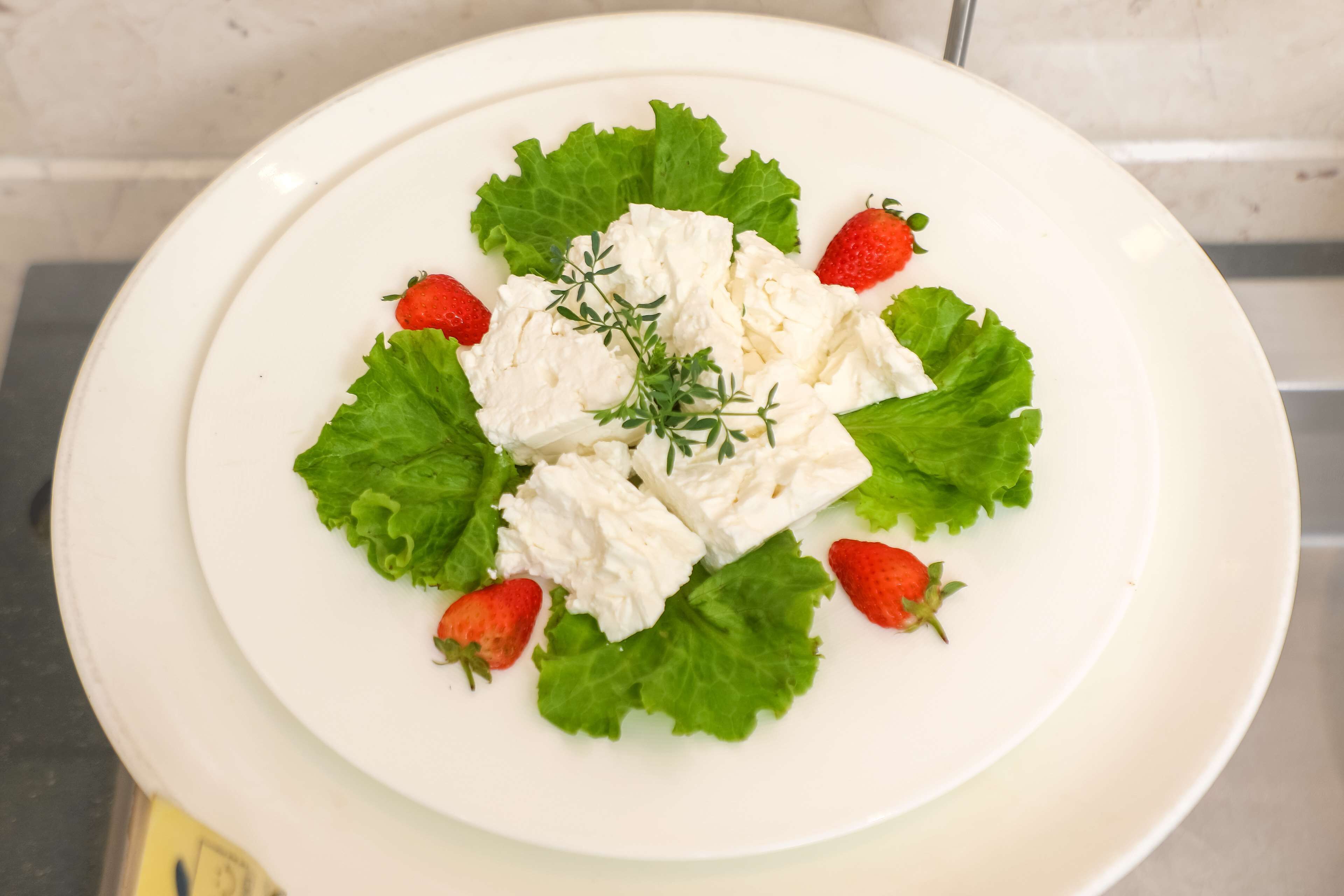 A white plate with a salad consisting of lettuce, strawberries, and a dollop of cream or cheese, garnished with a sprig of herbs.