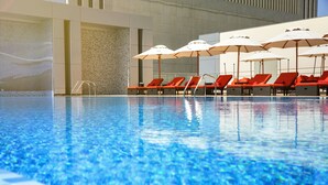 Una piscina amb aigua blava cristal·lina, envoltada de gandules vermelles i paraigües blancs.