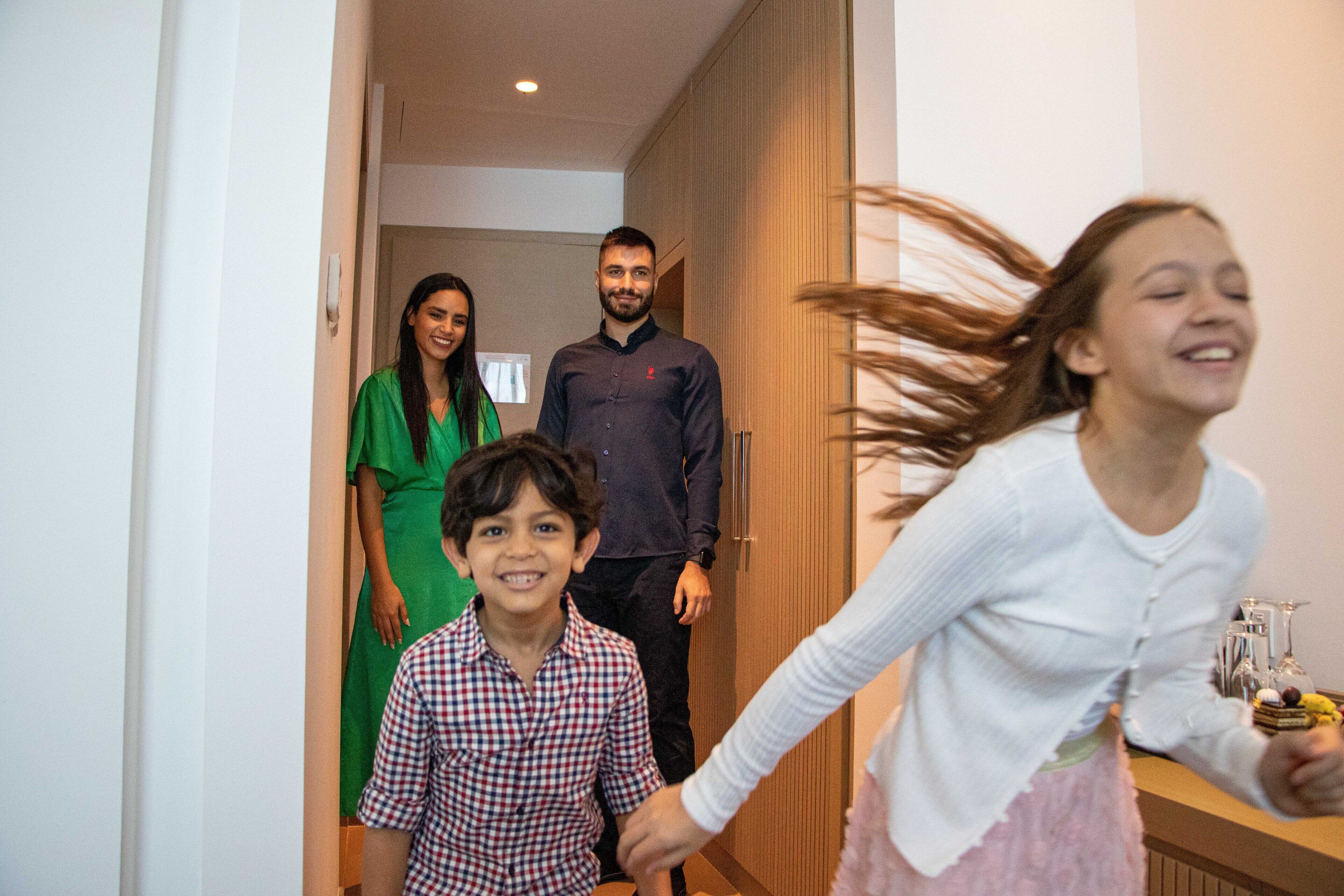 A family in a hallway with a wooden door and a plant.