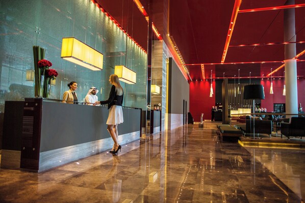 Zona de recepción de hotel con diseño moderno, que incluye un mostrador de recepción, área de estar y una pared de acento roja.