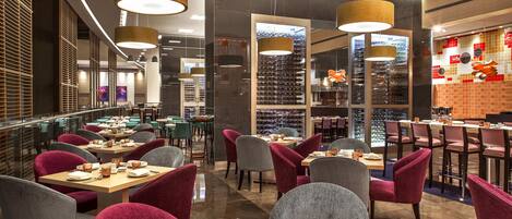 Interior moderno de restaurante com várias mesas de jantar, cadeiras e iluminação pendente.