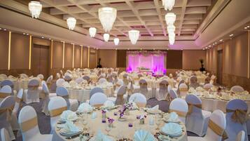 Ein Festsaal mit runden Tischen, festlich gedeckt für eine formelle Veranstaltung, mit weißen Tischdecken, goldenen Satinbändern und floralen Mittelstücken.