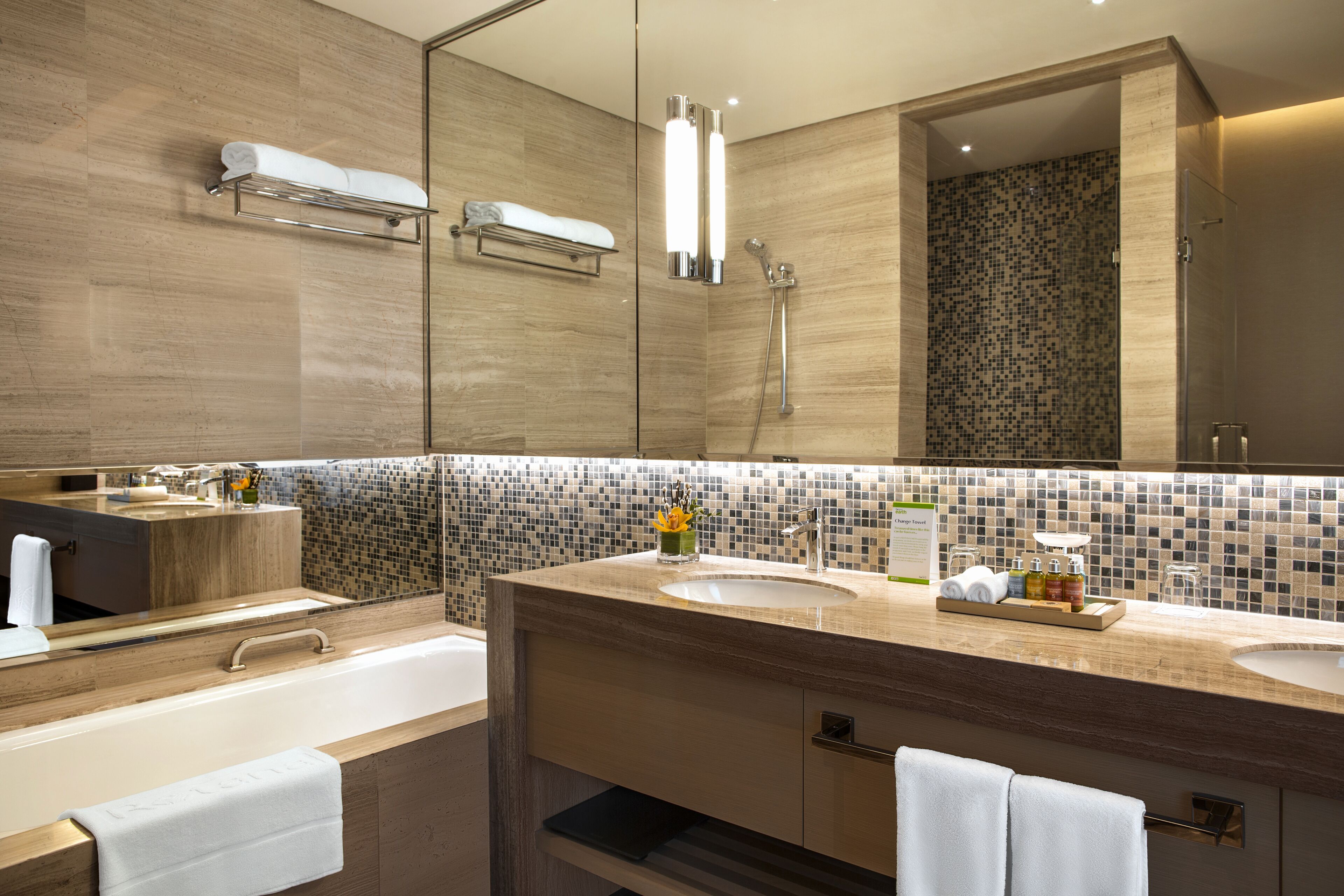 A modern bathroom with a large mirror, two sinks, a bathtub, and a shower area.