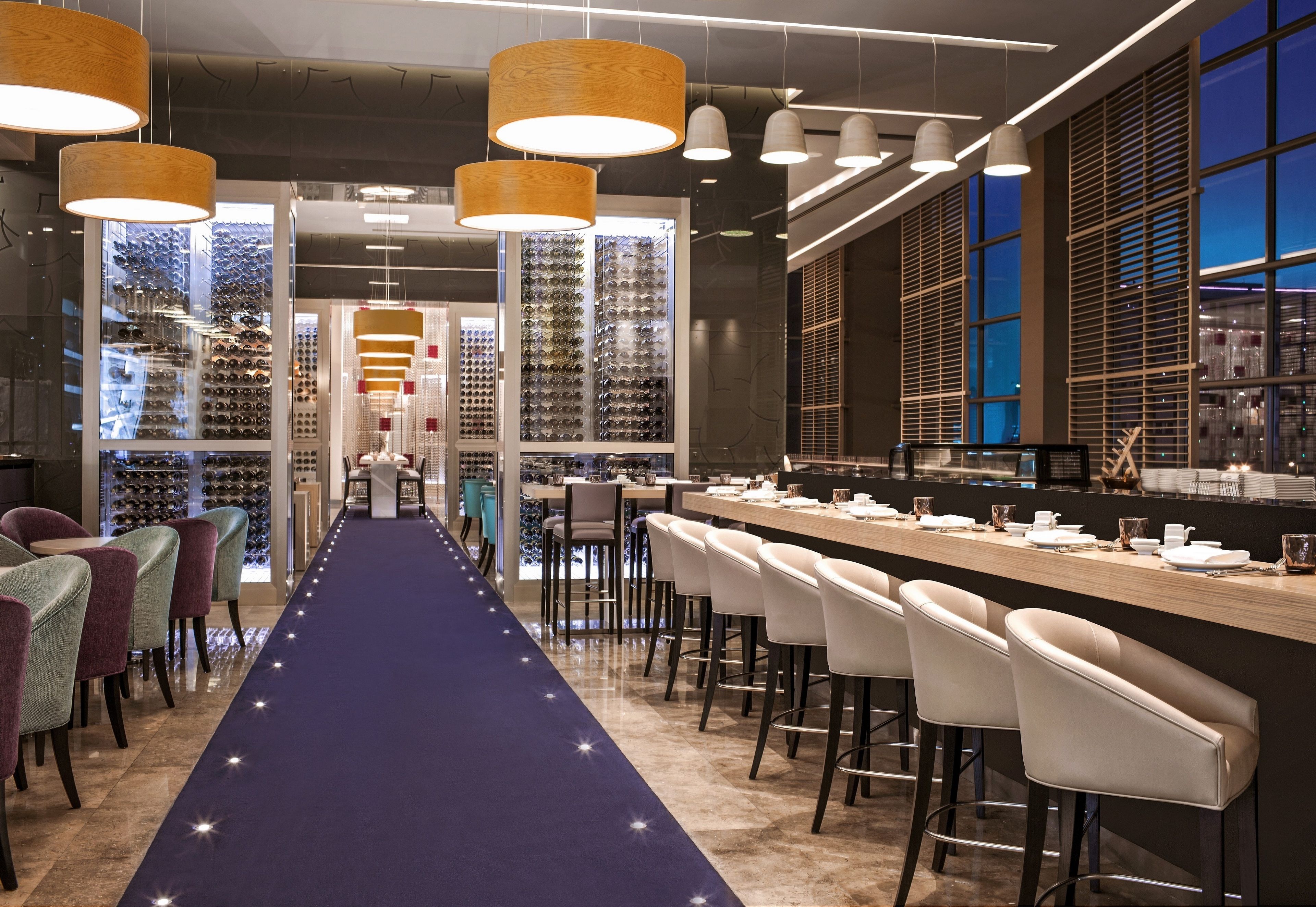 A modern bar area with a long counter, multiple bar stools, and hanging pendant lights.