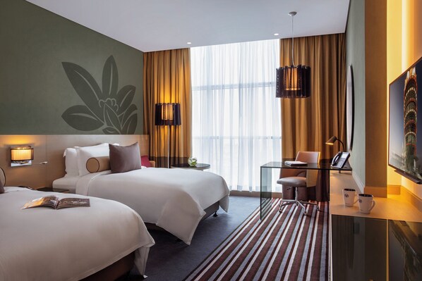 A hotel room with two beds, a desk with a chair, a glass coffee table, and a large window with curtains. - Downtown Rotana (Manama)
