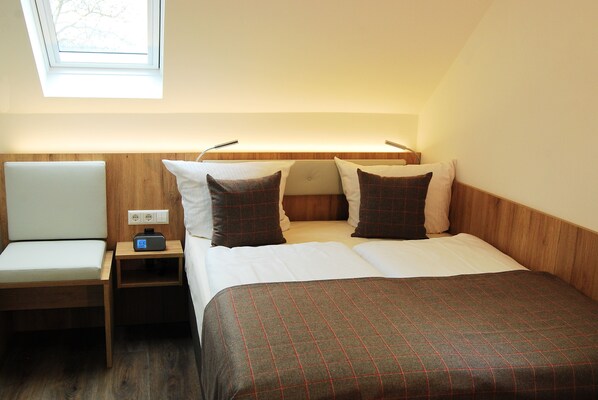 A hotel room with a bed, a bedside table with a lamp, a chair, and a window with a view of trees.