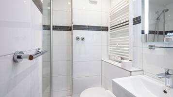 Un baño moderno con cabina de ducha de vidrio, inodoro blanco y lavamanos con espejo.
