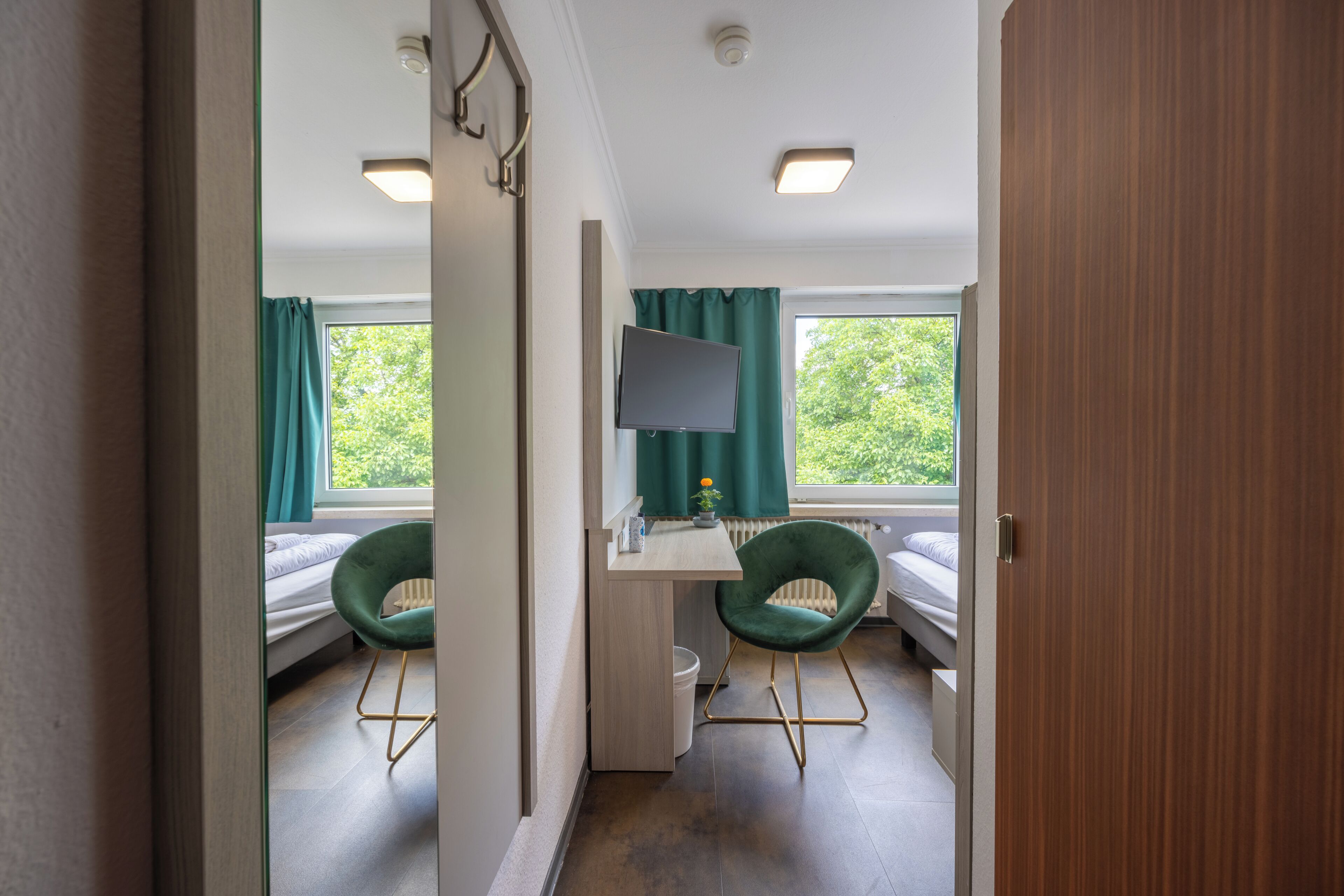 A room with a bed, two chairs, a desk with a computer, and a window with curtains.