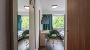 A room with a bed, two chairs, a desk with a computer, and a window with curtains.