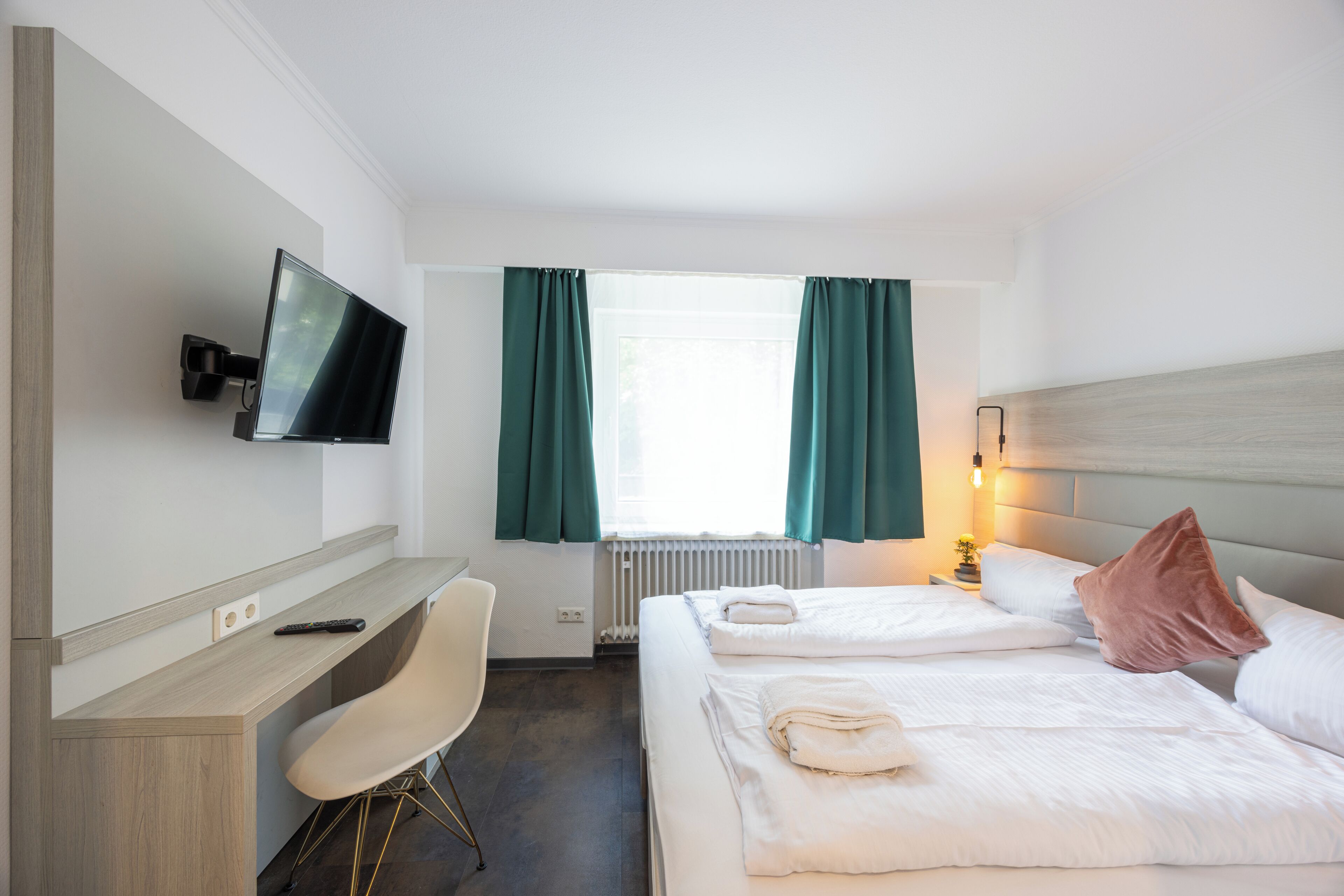 A hotel room with a bed, a desk, a chair, a TV, and a window with curtains.