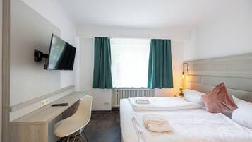 Ein Hotelzimmer mit Bett, Schreibtisch, Stuhl, Fernseher und einem Fenster mit Vorhängen.